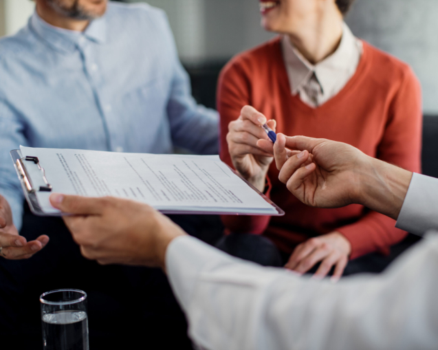 Close-up of woman signing an agreement with insurance agent while being on a meeting with her husband.